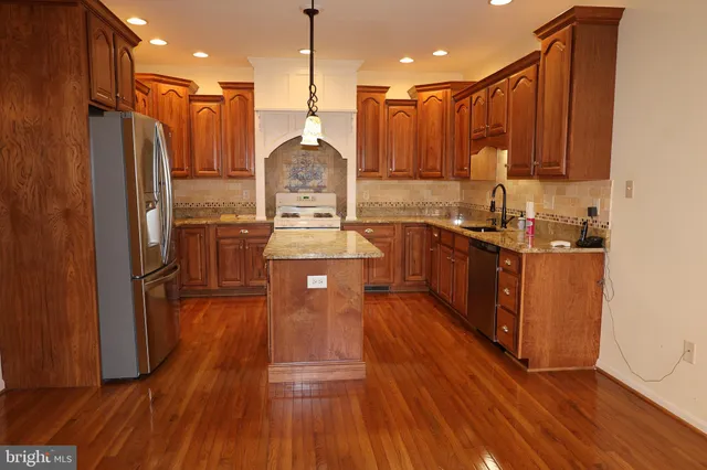 a kitchen with stainless steel appliances kitchen island granite countertop wooden floors wooden cabinets a sink and a stove