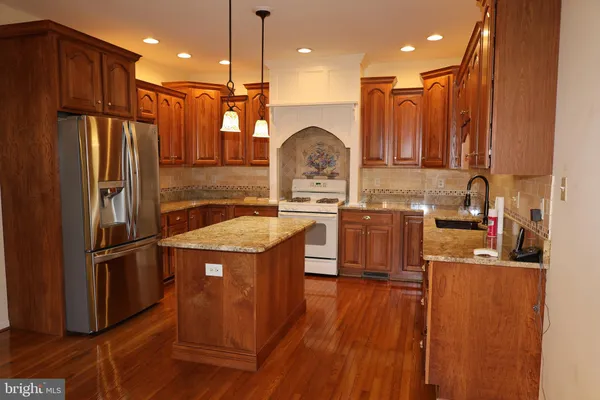 a kitchen with stainless steel appliances kitchen island granite countertop wooden floors wooden cabinets a sink and a stove