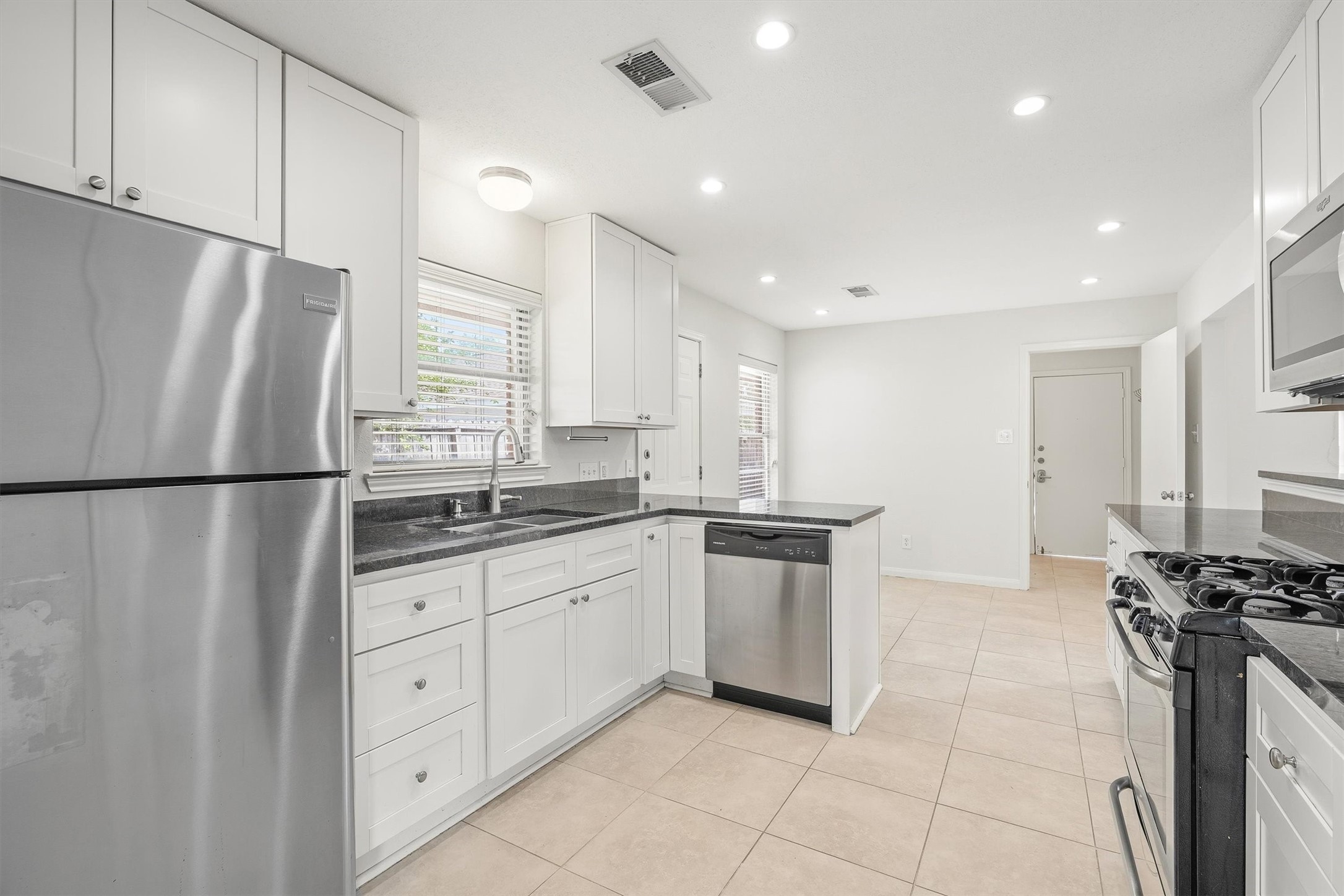 3331 Arbor Street Houston, TX 77004 - Photo 7 of 30 This modern kitchen features stainless steel appliances, white cabinetry, and a spacious layout with tile flooring. It's well-lit with natural light from the windows, creating an inviting cooking space.