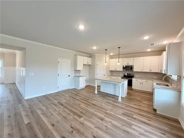 a large kitchen with kitchen island a stove a sink dishwasher a refrigerator and white cabinets with wooden floor