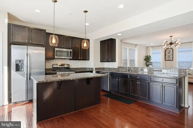 a kitchen with stainless steel appliances granite countertop a sink a stove a refrigerator cabinets and wooden floor