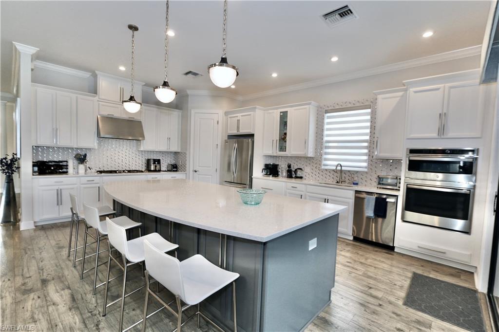 8337 Promoso Court Naples, FL 34114 - Photo 15 of 48 Kitchen featuring a breakfast bar, a kitchen island, decorative light fixtures, stainless steel appliances, and light stone counters