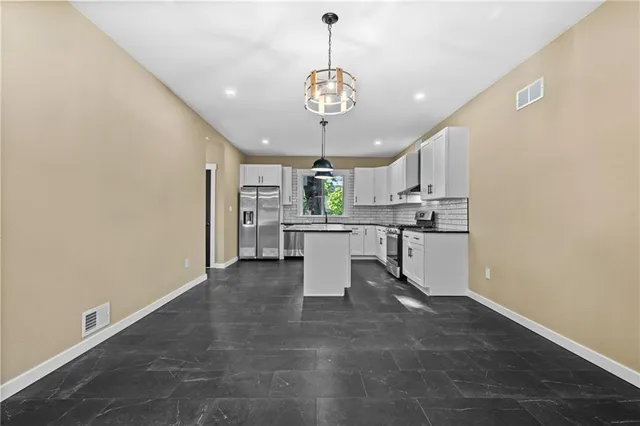 a kitchen with stainless steel appliances granite countertop a stove a sink dishwasher a refrigerator and white cabinets with wooden floor