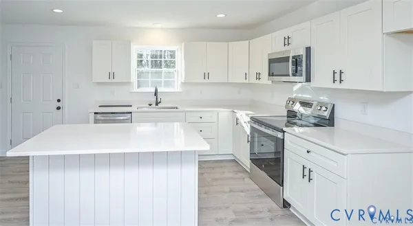 a kitchen with stainless steel appliances a sink dishwasher stove refrigerator and white cabinets with wooden floor