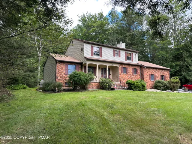 a view of a yard in front of a house with plants and large trees