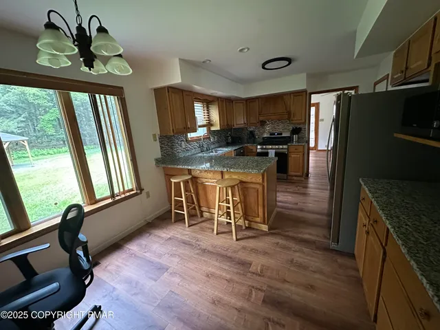 a kitchen with stainless steel appliances granite countertop a stove a refrigerator a sink a dining table and chairs with wooden floor