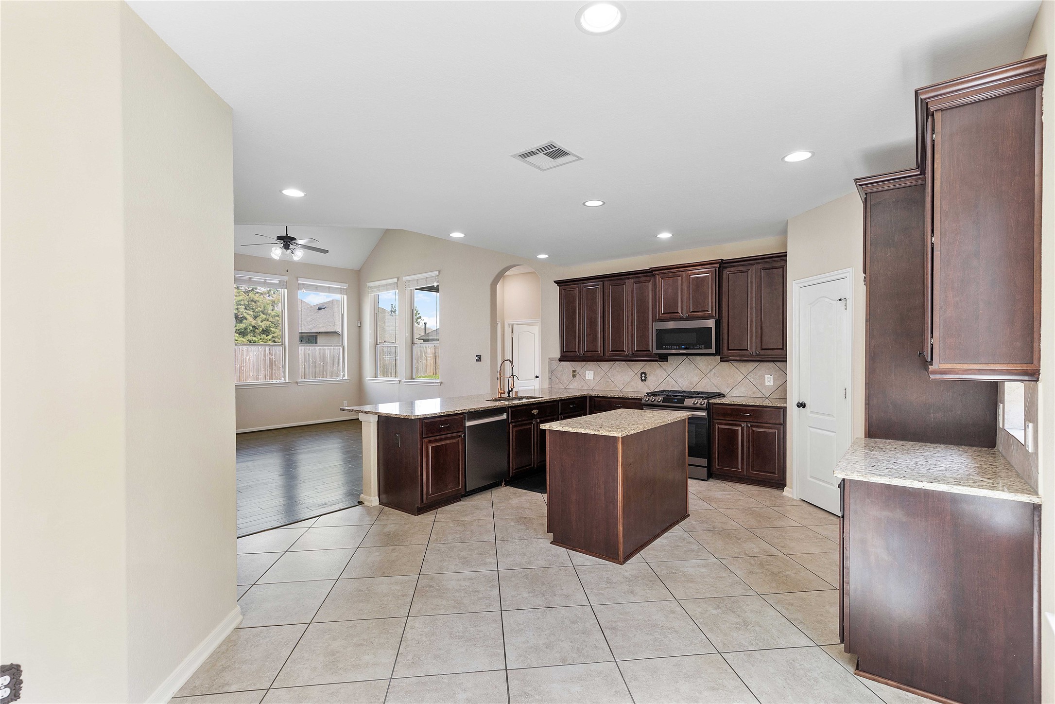 17206 Upper Ridge Lane Humble, TX 77346 - Photo 7 of 50 This spacious kitchen features dark wood cabinets, a central island, and tile flooring. It opens to a bright living area with large windows and a ceiling fan, offering a seamless flow for entertaining.