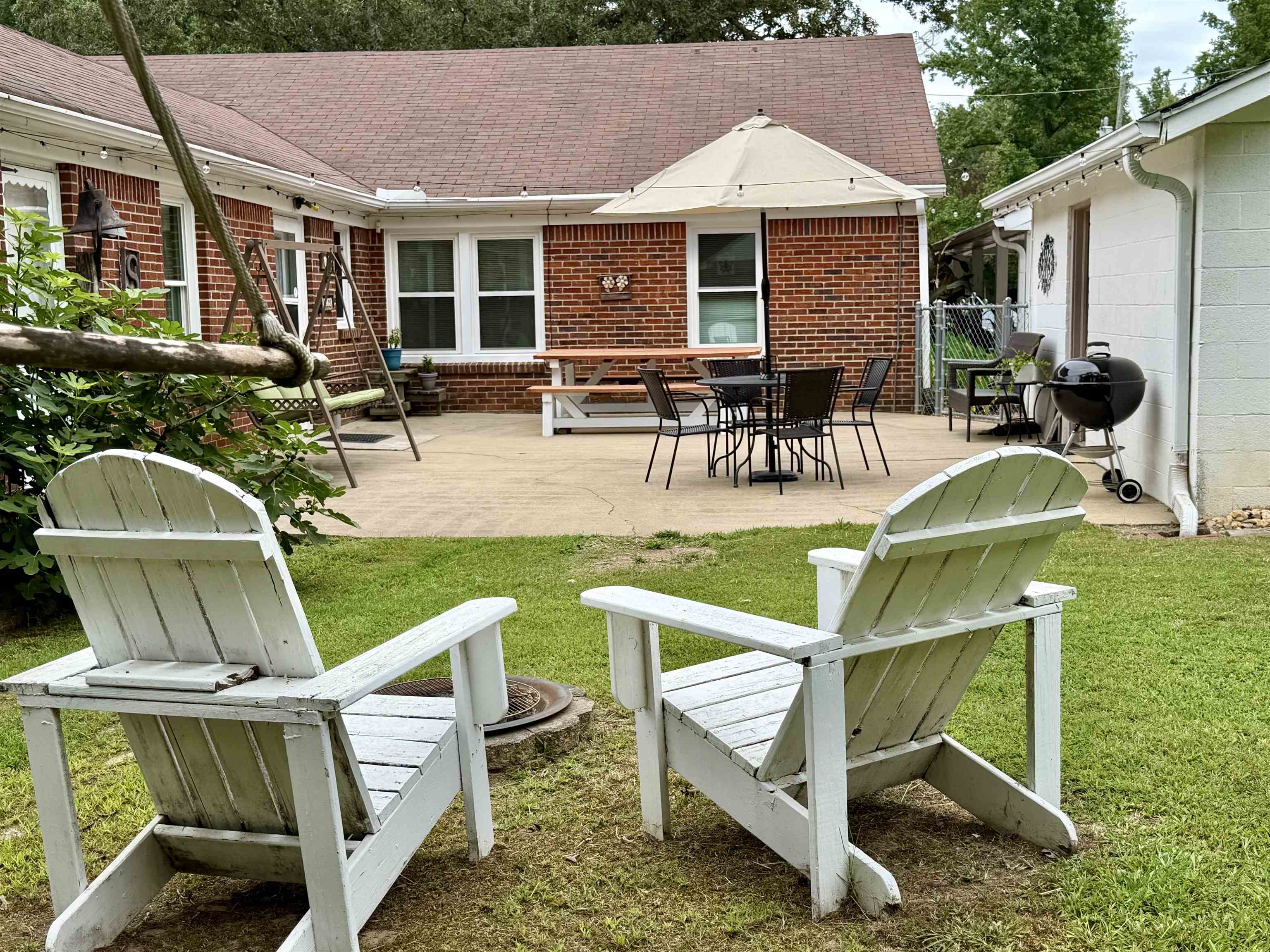 206 Burns Road Ramer, TN 38367 - Photo 24 of 37 Expansive concrete patio with ample outdoor living space, featuring a brick exterior, white framed windows, and a mature green lawn