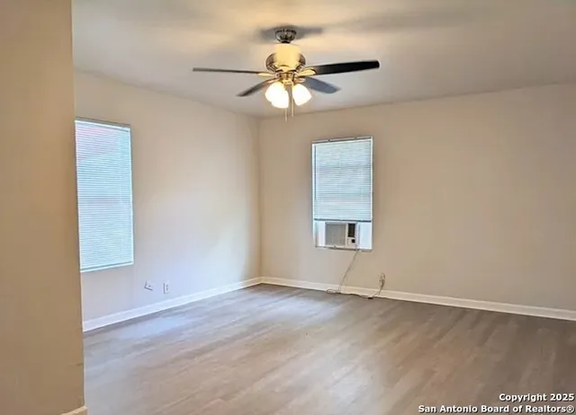an empty room with wooden floor chandelier fan and windows