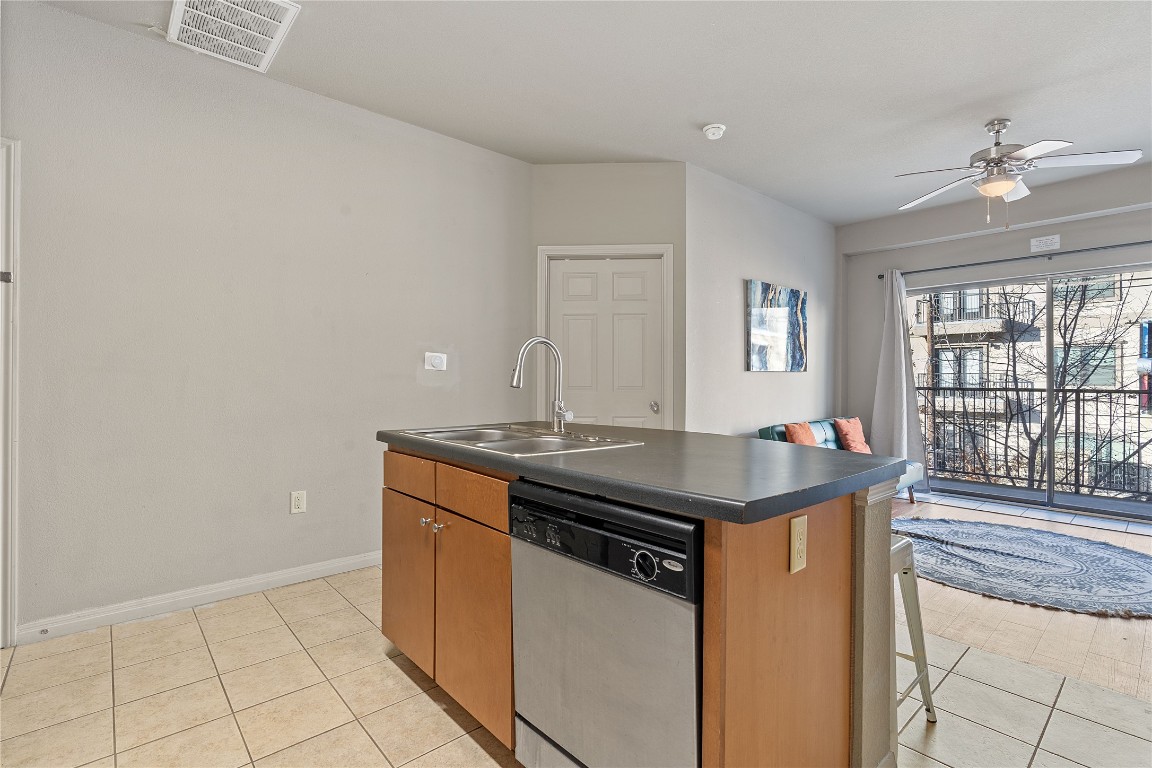 2515 Pearl Street, Unit 404 Austin, TX 78705 - Photo 12 of 17 Kitchen with an island with sink, stainless steel dishwasher, light tile patterned flooring, brown cabinets, and a ceiling fan