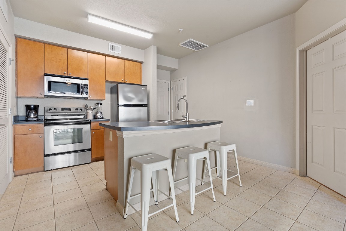 2515 Pearl Street, Unit 404 Austin, TX 78705 - Photo 13 of 17 Kitchen featuring appliances with stainless steel finishes, a kitchen breakfast bar, light tile patterned flooring, a kitchen island with sink, and dark countertops