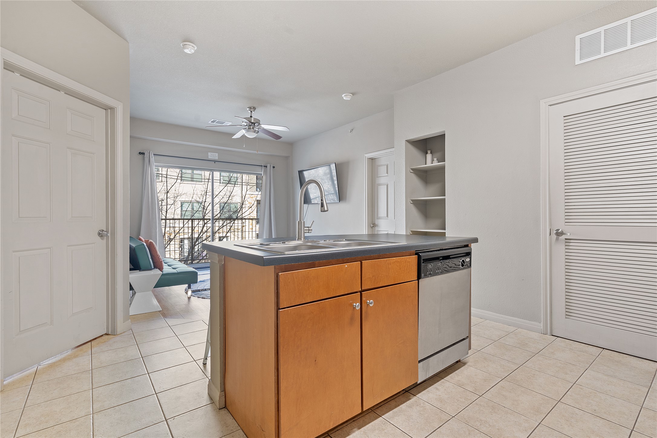 2515 Pearl Street, Unit 314 Austin, TX 78705 - Photo 10 of 17 Kitchen featuring brown cabinets, light tile patterned flooring, an island with sink, a ceiling fan, and dishwasher
