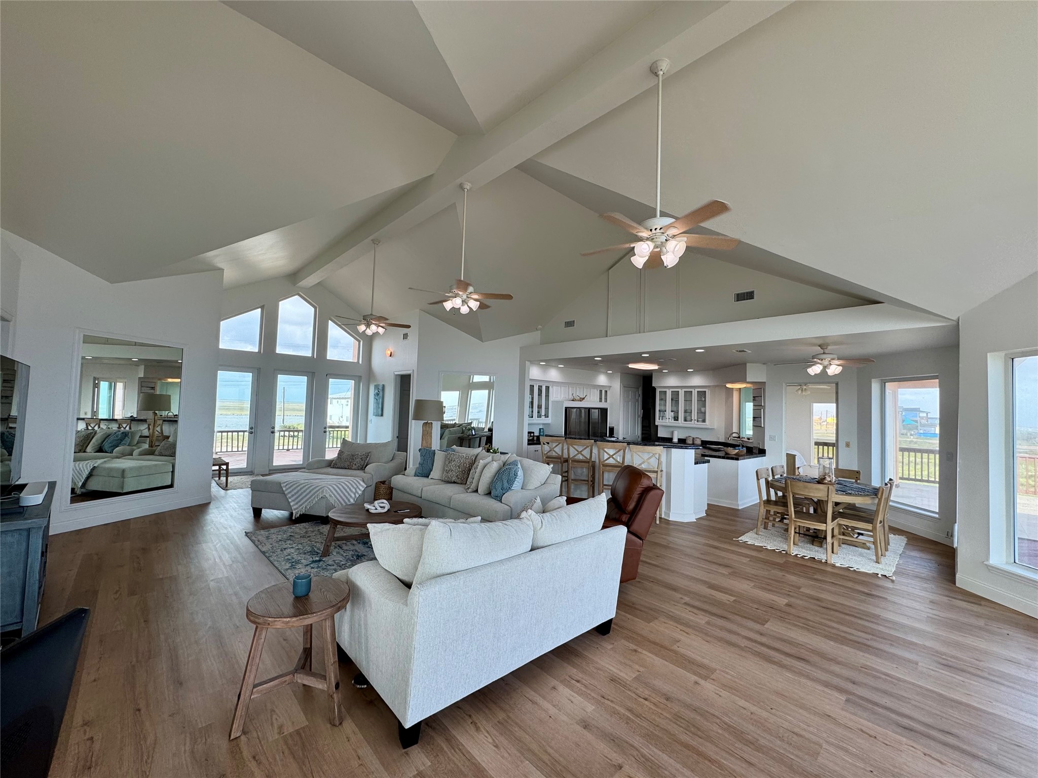 878 County Road 230 Sargent, TX 77414 - Photo 18 of 39 This spacious open-concept living area features high vaulted ceilings, abundant natural light from large windows, a modern kitchen with a dining area, and stylish wood flooring. Perfect for entertaining and enjoying scenic views.