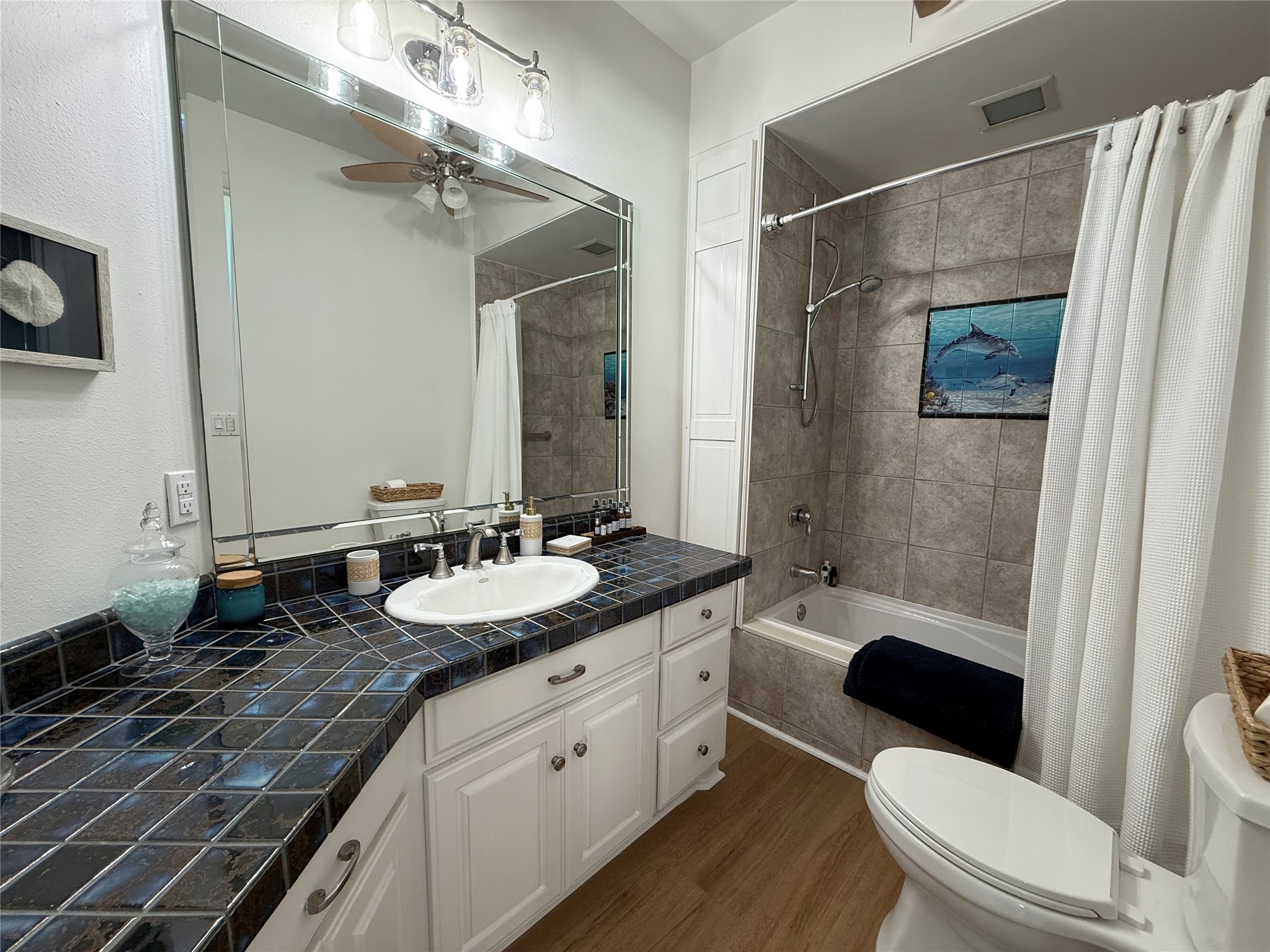 878 County Road 230 Sargent, TX 77414 - Photo 24 of 39 This bathroom features a stylish design with a large mirror. It includes a shower-tub combo with tile surround, modern fixtures, and wood flooring, creating a clean and inviting space.