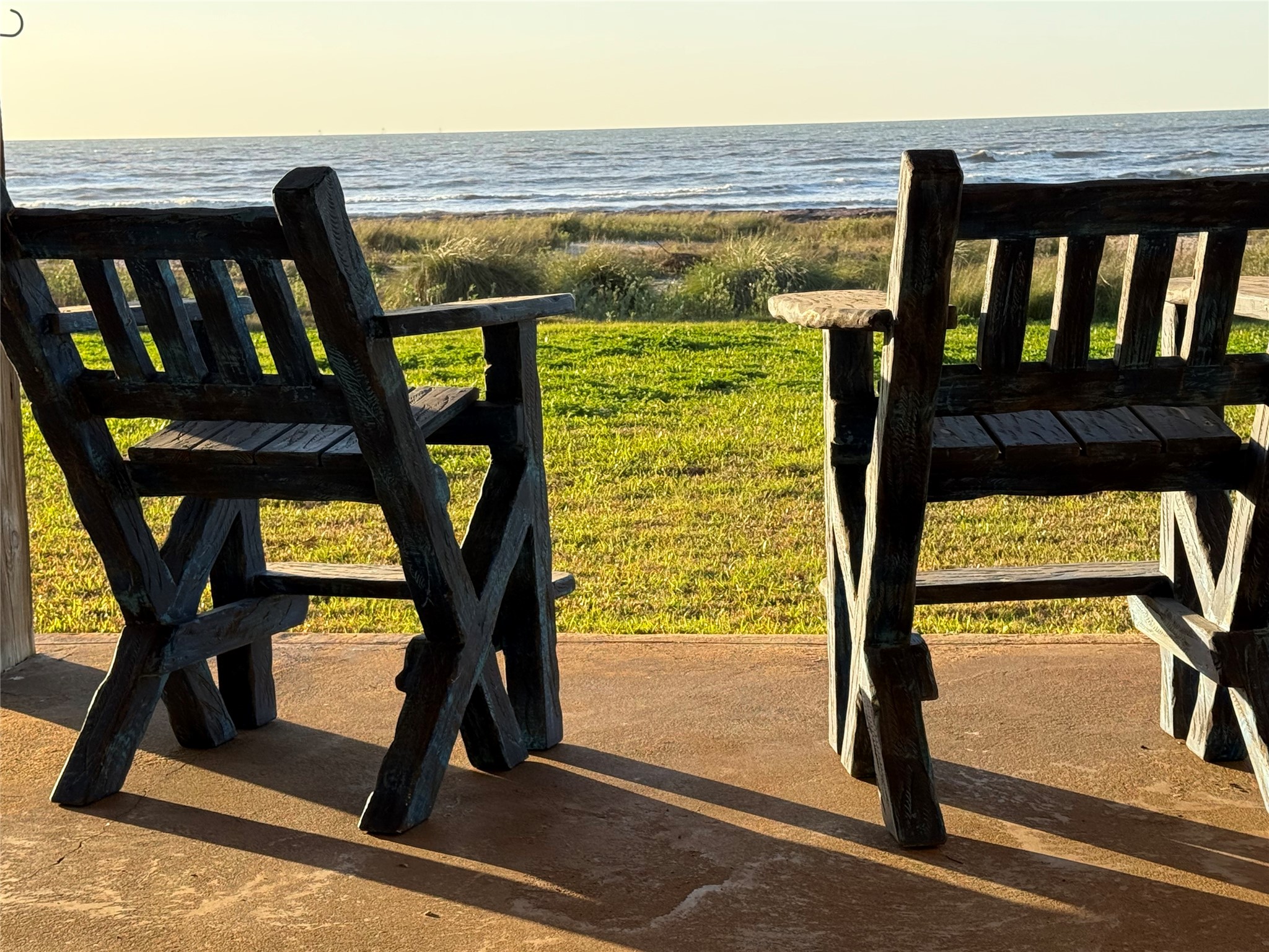 878 County Road 230 Sargent, TX 77414 - Photo 33 of 39 A serene oceanfront view from the covered area under the home overlooking lush grass and the sea, perfect for relaxation and enjoying sunsets.