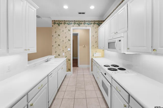 a large white kitchen with granite countertop a sink a stove refrigerator and cabinets