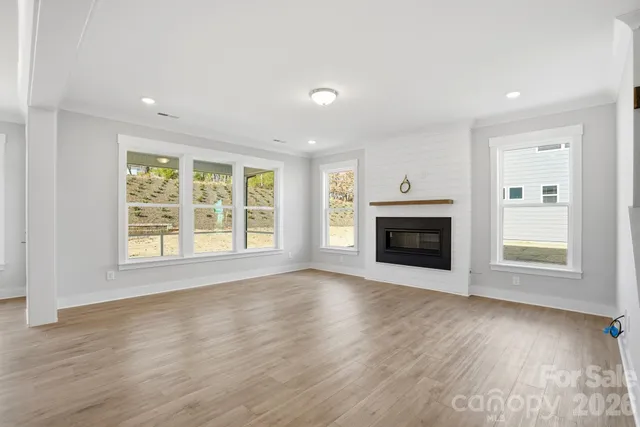 an empty room with wooden floor fireplace and windows