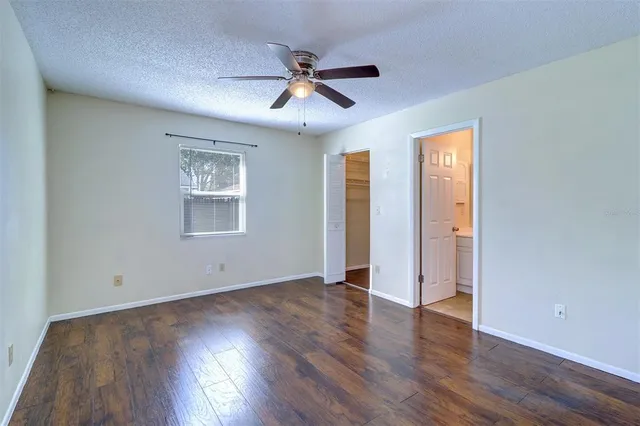 a view of an empty room with wooden floor and a ceiling fan