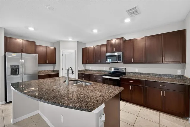 a kitchen with kitchen island granite countertop stainless steel appliances a sink a stove a microwave a sink a refrigerator and cabinets