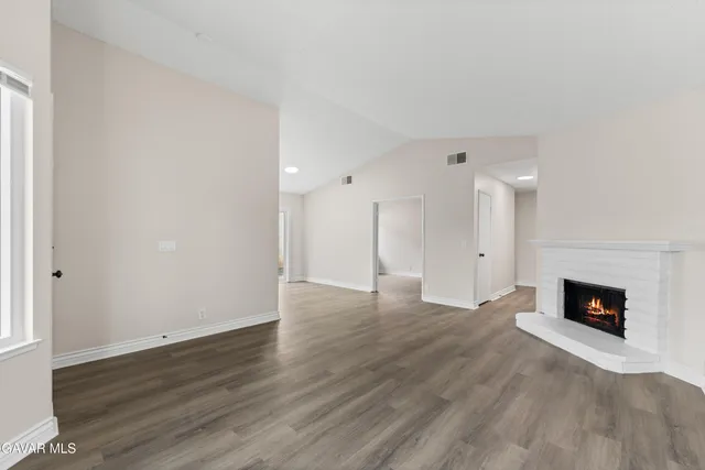 a view of an empty room with wooden floor and a fireplace