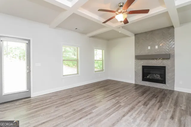 an empty room with windows a fireplace a ceiling fan and wooden floor