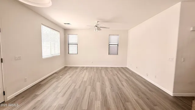 an empty room with wooden floor ceiling fan and windows