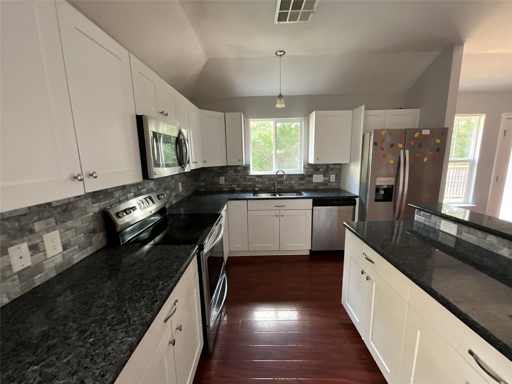 239 Old Firetower Road Bastrop, TX 78602 - Photo 23 of 39 Kitchen featuring appliances with stainless steel finishes, dark stone counters, white cabinets, dark wood-style floors, and decorative backsplash and center island