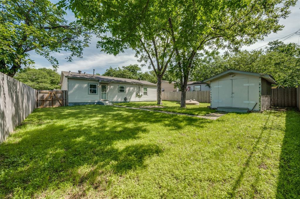 2316 Cunningham Street Irving, TX 75062 - Photo 20 of 22 Expansive backyard featuring a large green space, mature shade trees, a detached storage shed, a wood privacy fence, and a gate entrance