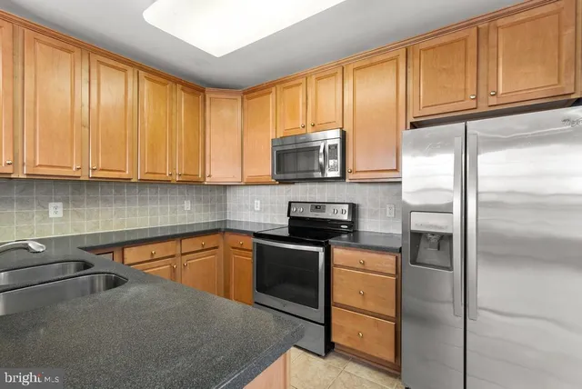 a kitchen with stainless steel appliances granite countertop a refrigerator a stove a sink and dishwasher with wooden floor