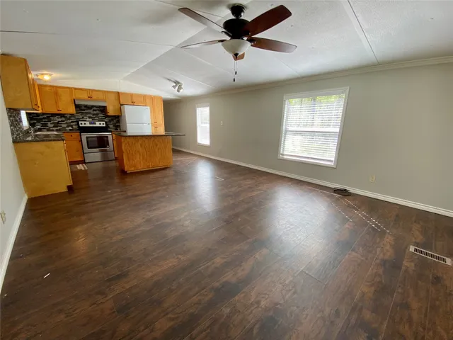 an empty room with wooden floor kitchen view and a window