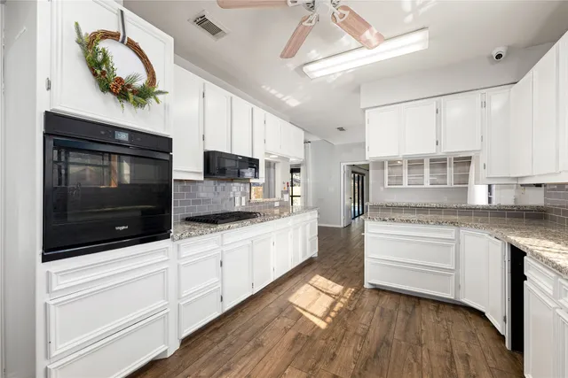 a kitchen with stainless steel appliances white cabinets a sink a stove a microwave and wooden floors