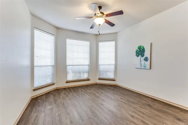 an empty room with wooden floor chandelier fan and windows