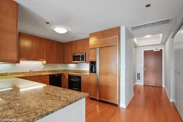 a kitchen with stainless steel appliances granite countertop a refrigerator a sink dishwasher a stove and white countertops with wooden floor