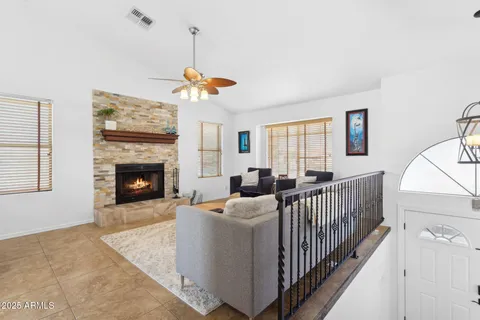 a view of a livingroom with furniture a fireplace a ceiling fan and windows