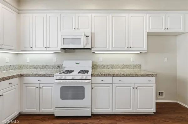 a kitchen with granite countertop white cabinets white appliances a sink and a window