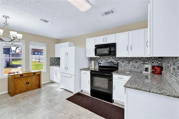 a kitchen with stainless steel appliances granite countertop a stove top oven a sink a refrigerator and white cabinets with wooden floor