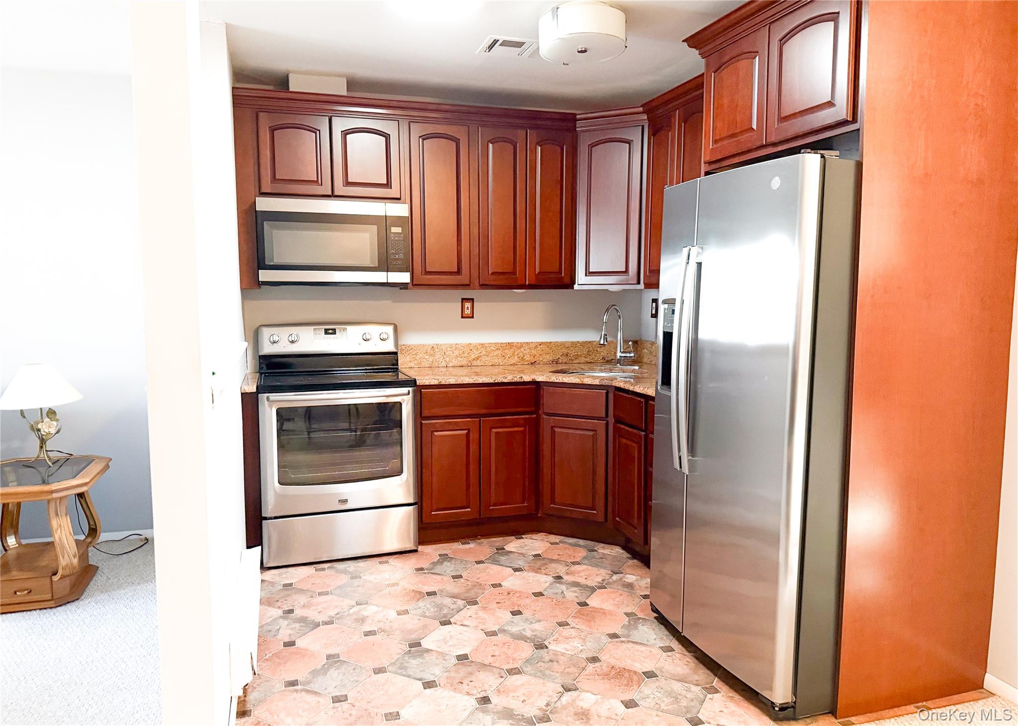 423 Woodbridge Drive, Unit B Ridge, NY 11961 - Photo 5 of 13 Kitchen featuring stainless steel appliances, light flooring, light stone counters, and brown cabinetry
