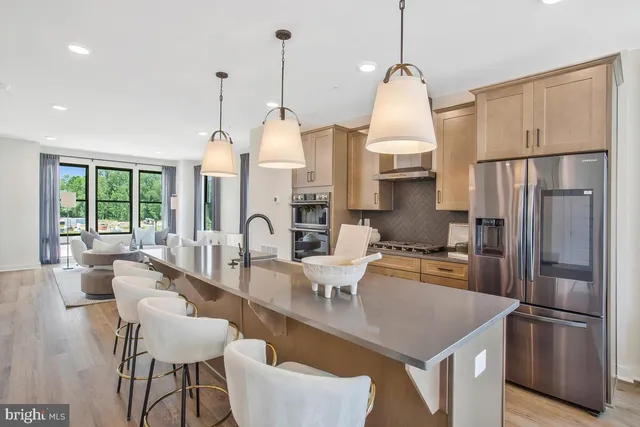 a kitchen with stainless steel appliances granite countertop a refrigerator a sink dishwasher a stove and a dining table with wooden floor