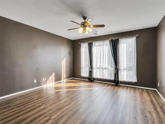 an empty room with wooden floor fan and windows