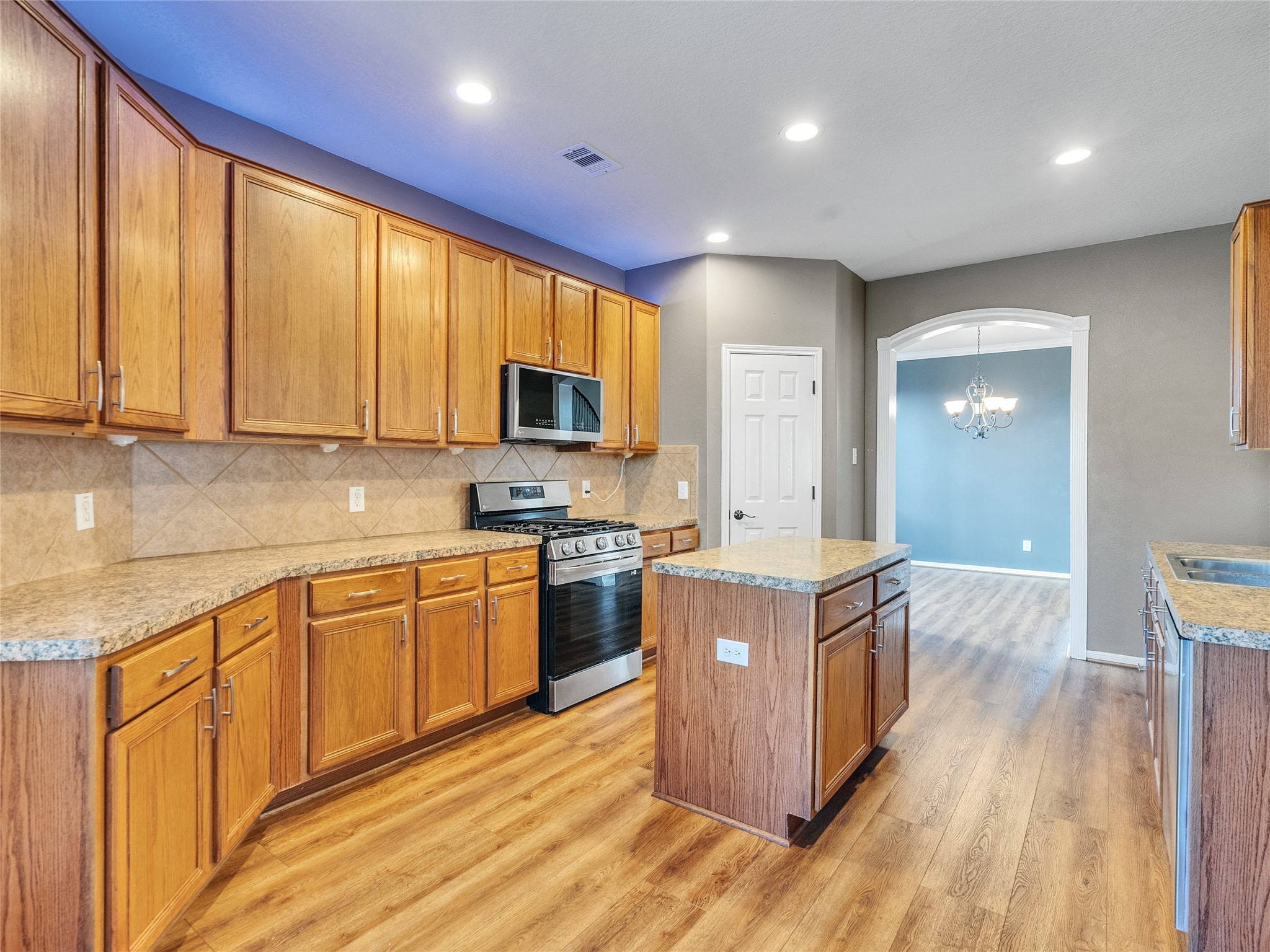 9915 Valance Way Conroe, TX 77385 - Photo 9 of 31 a kitchen with kitchen island granite countertop a stove top oven a sink dishwasher and wooden cabinets with wooden floor