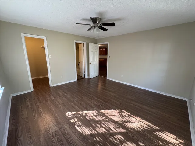a view of an empty room with wooden floor and a ceiling fan