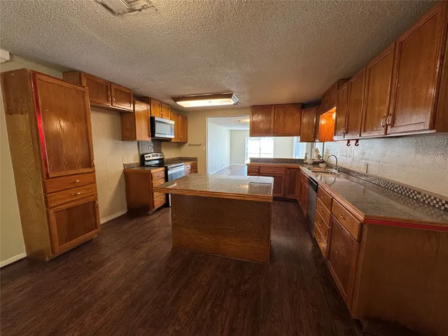 a kitchen with granite countertop stainless steel appliances a sink a refrigerator a window and cabinets