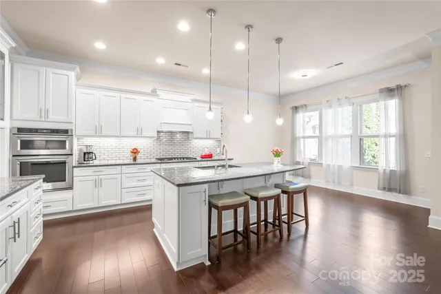a kitchen with stainless steel appliances granite countertop a table chairs wooden floors and white cabinets