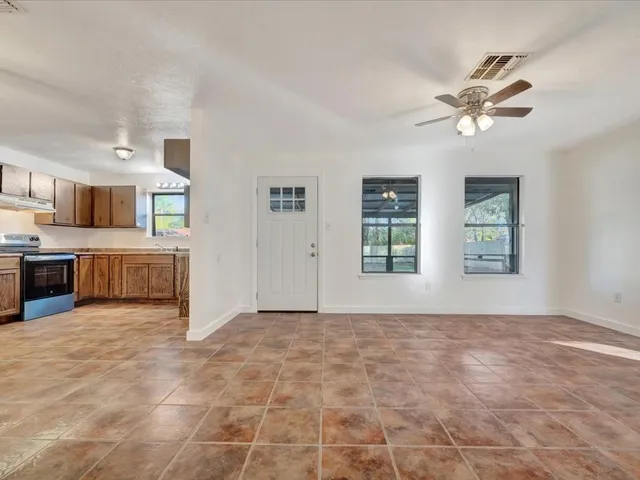 a view of a livingroom with kitchen appliances and a ceiling fan