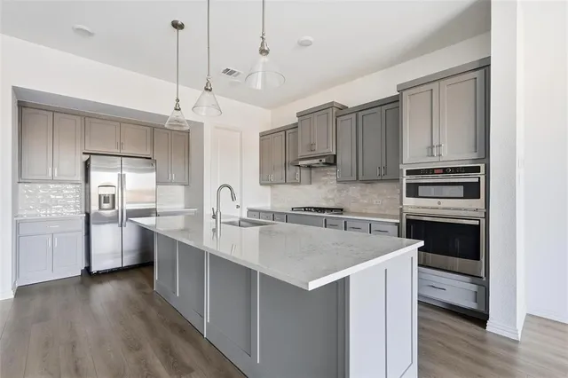 a kitchen with stainless steel appliances granite countertop a sink a oven a dining table and chairs with wooden floor