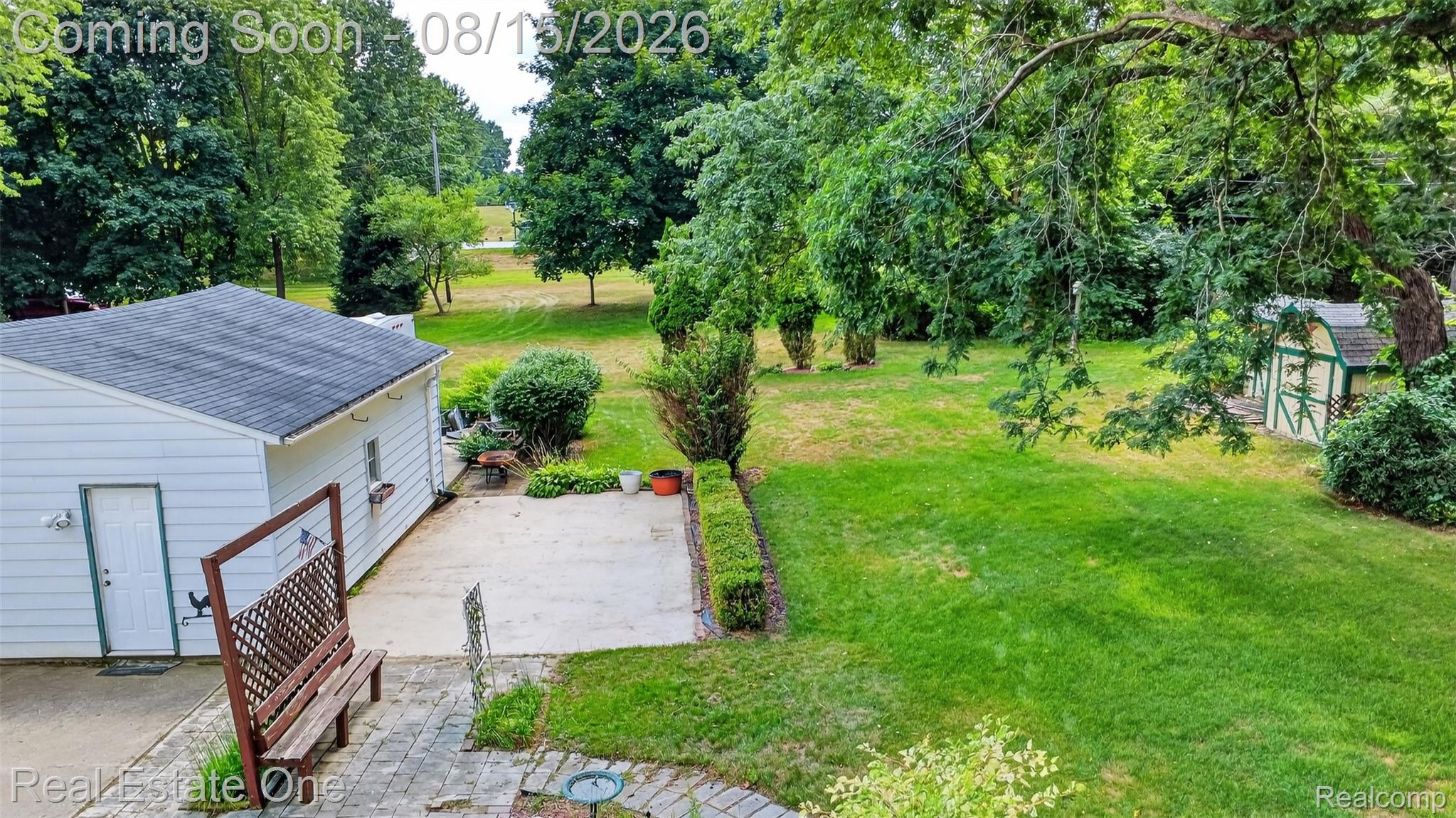 454 South Baldwin Road Oxford, MI 48371 - Photo 60 of 64 Expansive green space featuring mature trees, a detached structure with white siding and an asphalt shingle roof, a concrete patio area, and a separate storage shed