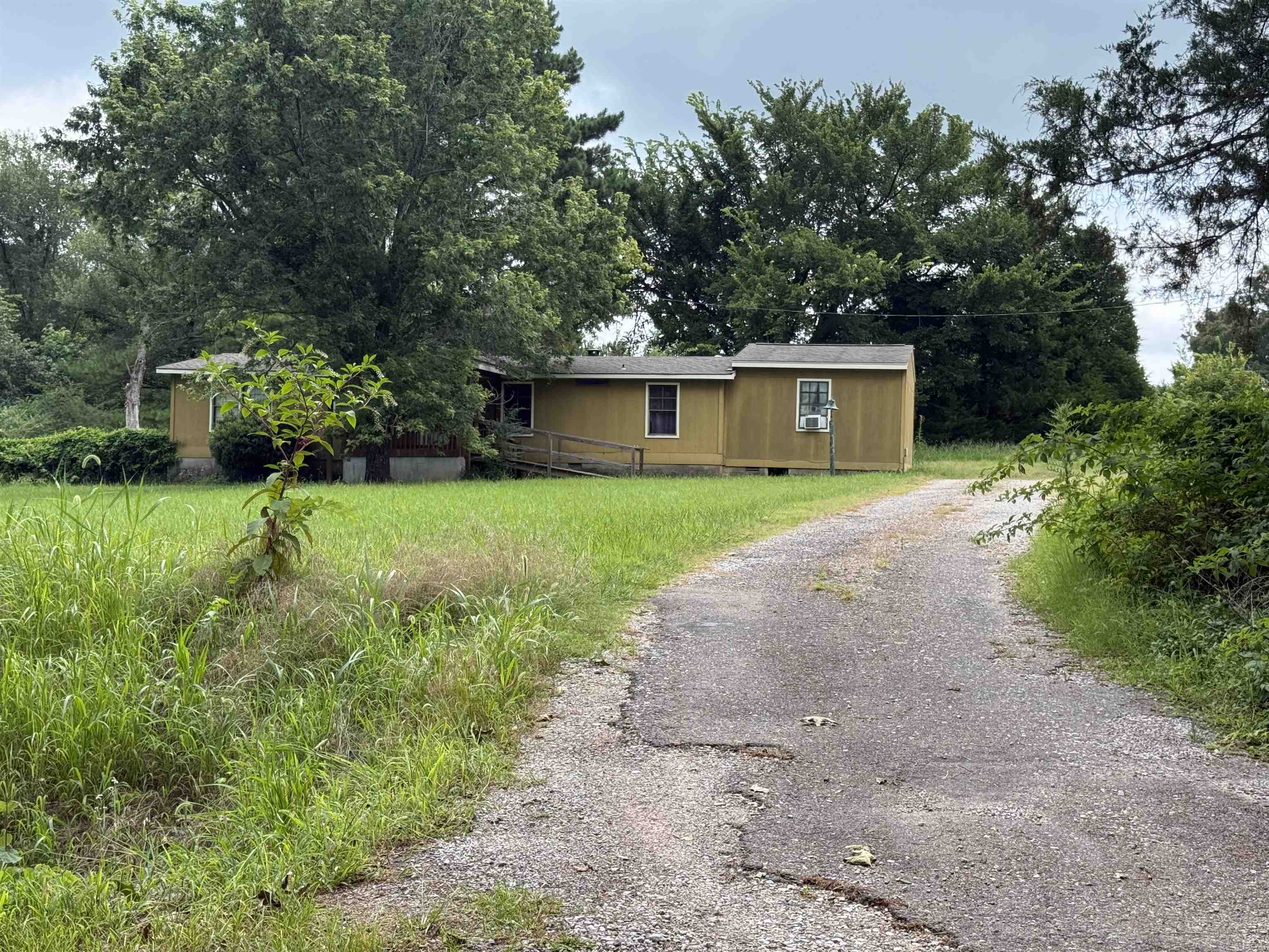 Single-story residence featuring light yellow siding, a gravel driveway, and a natural grass yard
