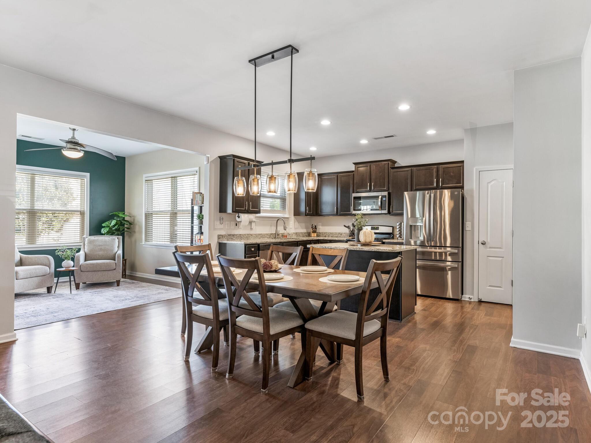 a kitchen with stainless steel appliances granite countertop a stove a refrigerator a kitchen island a dining table and chairs with wooden floor