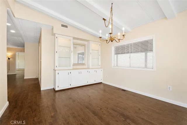 an empty room with wooden floor chandelier and windows