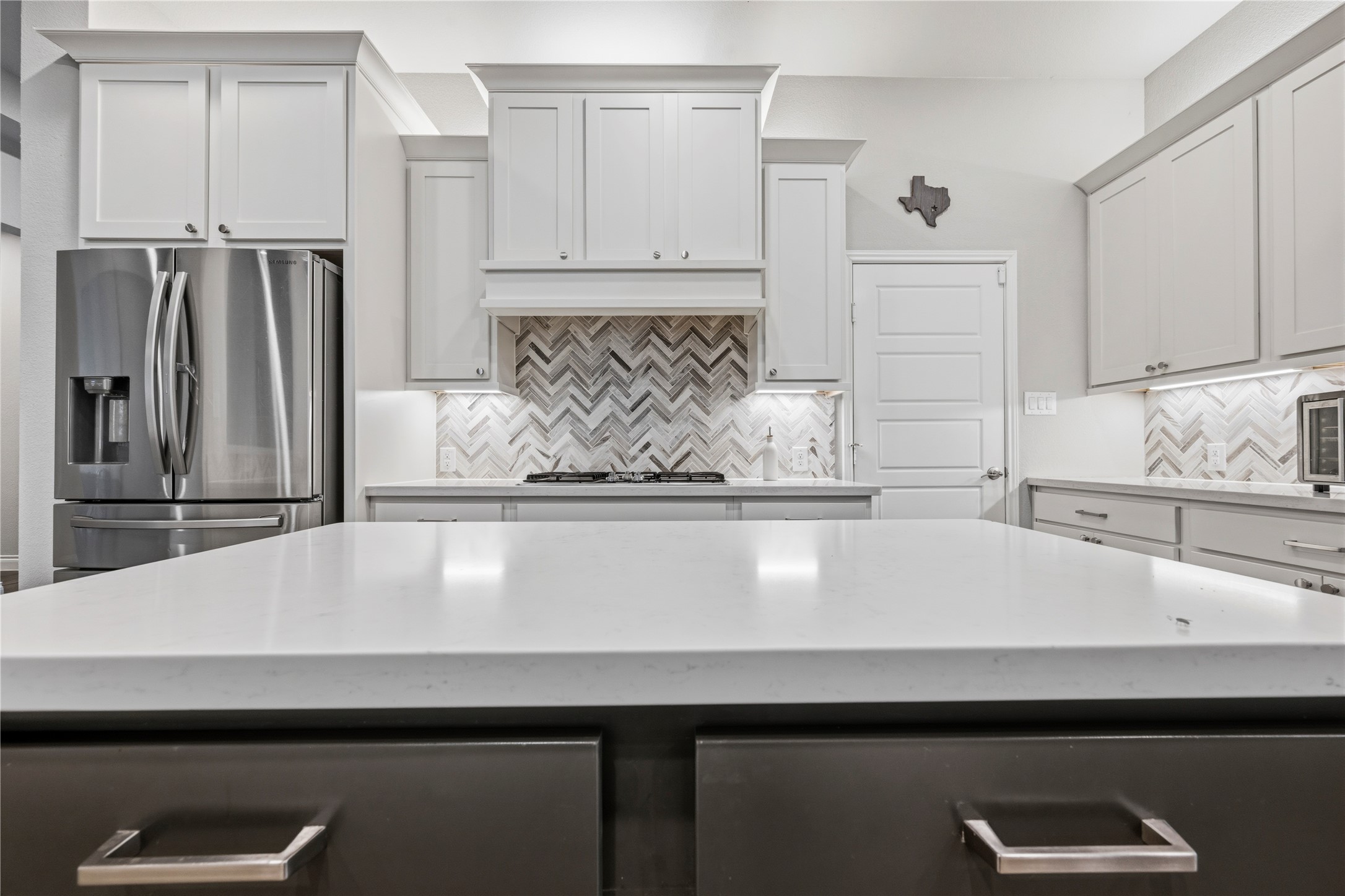 140 Catani Loop Georgetown, TX 78628 - Photo 17 of 36 White cabinetry, sleek countertops, and a herringbone tile backsplash create a crisp and elegant kitchen space.